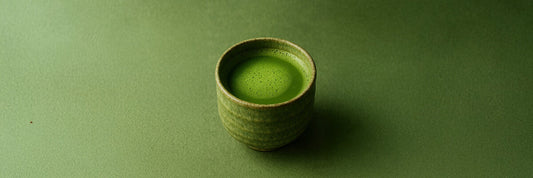 A bowl of frothy Usucha matcha green tea prepared in a traditional Japanese chawan on a green background.